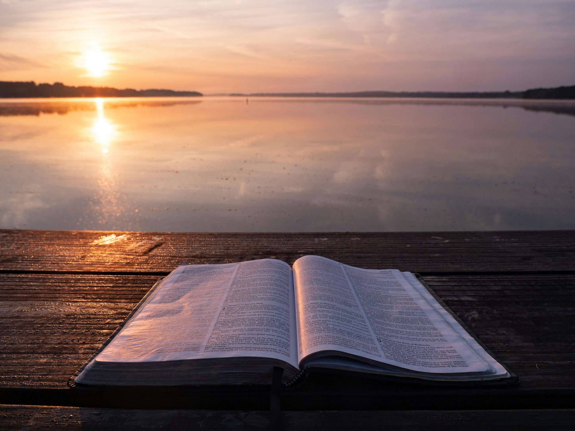Open Bible on a wooden deck by the water at sunset, symbolizing faith, reflection, and aligning business with biblical principles