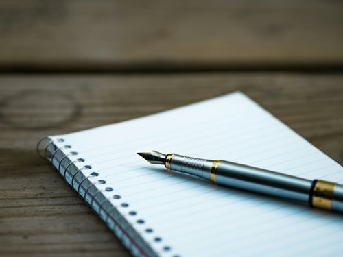 Fountain pen resting on lined spiral notebook, symbolizing reflection, goal setting, and personal development through writings