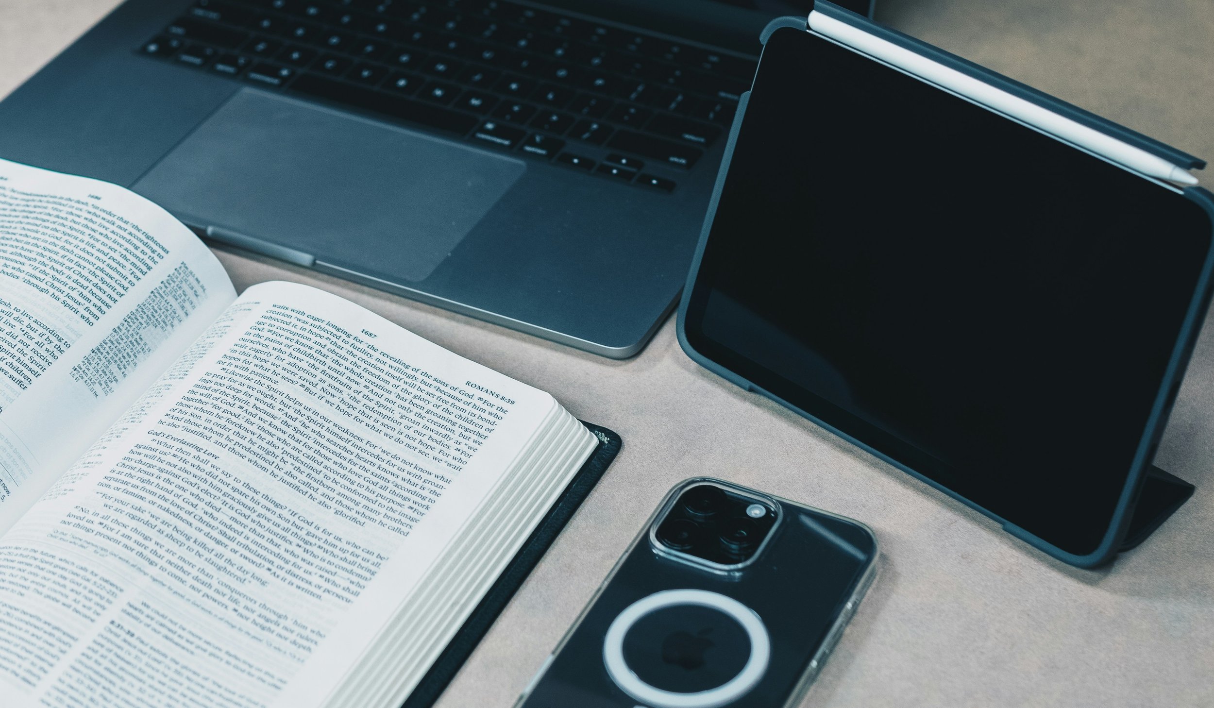 Bible beside laptop and smartphone on desk, representing the connection between Christian values, business leadership, and everyday work life