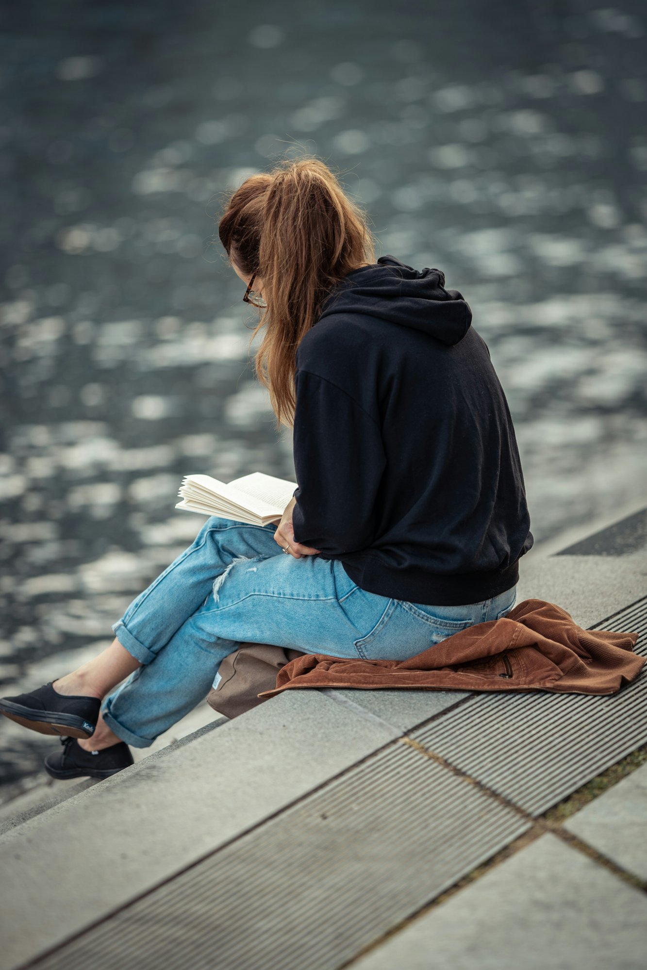 Woman enjoying quiet time by the water with a book on personal growth and success